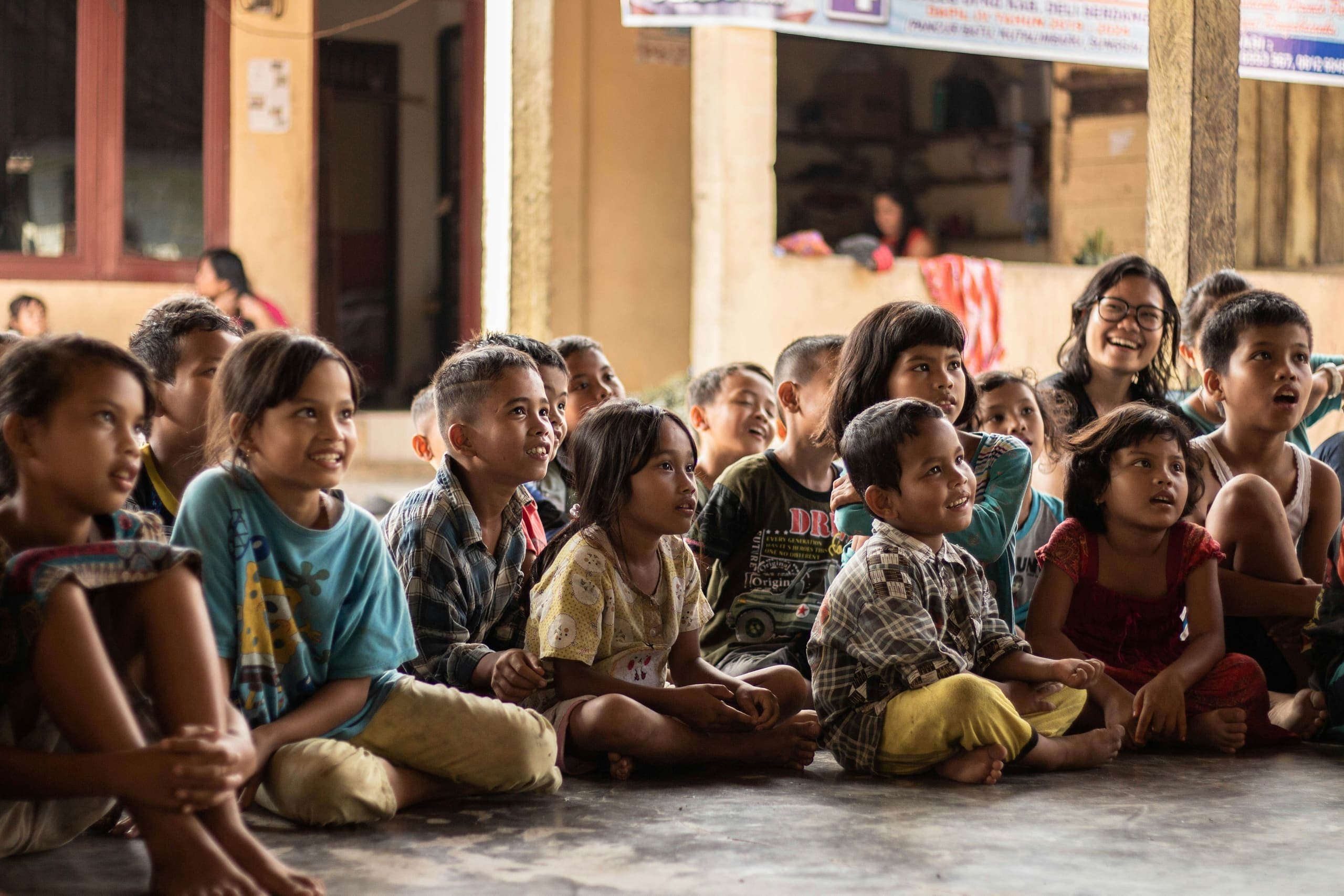 Children sitting together on the floor, smiling and listening
